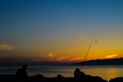 Silhouette people fishing at sea against sky during sunset