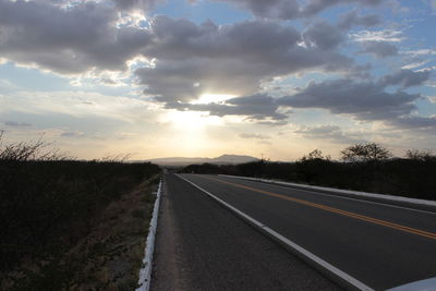 Road passing through field against cloudy sky