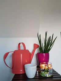 Tea light candle with watering can and houseplant on table against wall