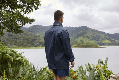 Rear view of man standing by lake against sky