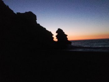 Silhouette trees on beach against clear sky