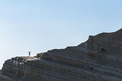 Low angle view of man standing on large rock against clear sky