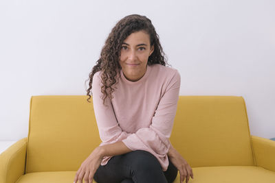 Portrait of a smiling young woman sitting on sofa against wall