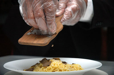 Close-up of hand shaving black truffle on pasta