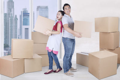 Portrait of couple carrying cardboard boxes while standing in new home