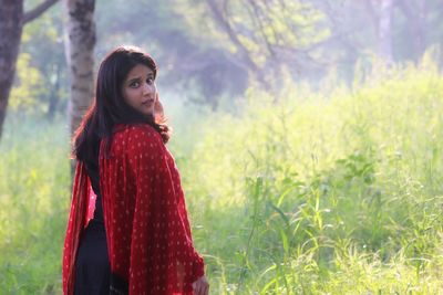 Young woman standing on field against trees