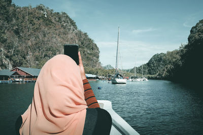 Rear view of woman photographing while sitting on boat in river