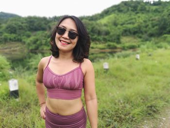 Smiling young woman standing on grass against sky