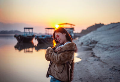 Woman standing by sea against sky during sunset