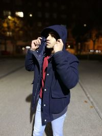 Young man wearing hooded jacket standing on street at night