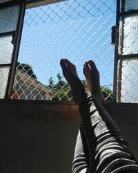 Low section of person against sky seen through fence