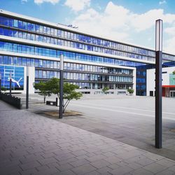 Empty sidewalk by modern buildings against sky