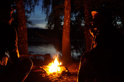 Couple sitting by bonfire during night in forest