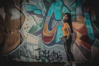 Full length of young woman standing against graffiti wall