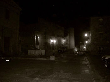 Empty road by illuminated buildings in city at night