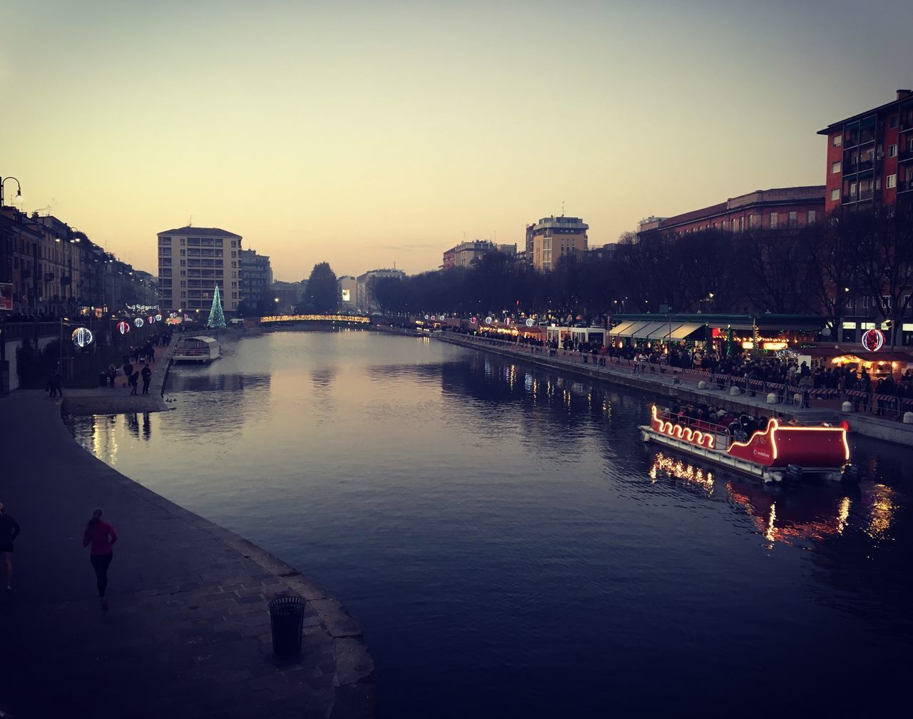 ILLUMINATED BRIDGE OVER RIVER BY BUILDINGS AGAINST SKY AT SUNSET