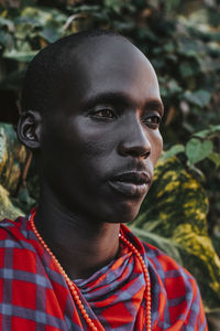 Maasai man in traditional clothes standing in front of green leaves
