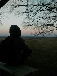 Rear view of man sitting on field against sky