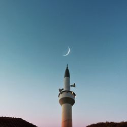 Low angle view of lighthouse against buildings against clear blue sky