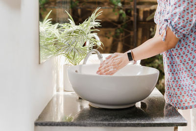 Woman washing hands with tap water under faucet at white sink