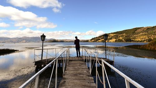 Man standing on railing against sky