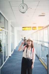 Portrait of young woman pointing up while standing at airport