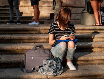 Full length of teenage girl using mobile phone while sitting on steps