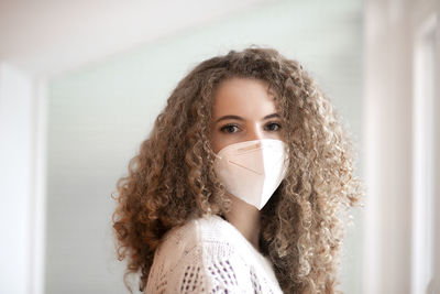 Portrait of young woman with curly hair and sad eyes in white color medical protective face mask 