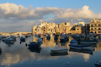 Boats moored at harbor in city against sky