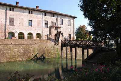 Old bridge over canal by building against sky