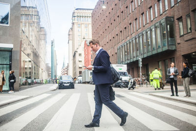 Mature businessman using phone while walking on zebra crossing in city