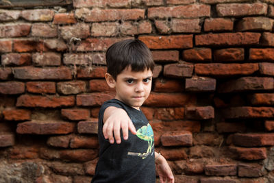 Portrait of boy gesturing against brick wall