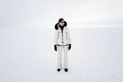 Full length of woman in warm clothing standing on snow covered field