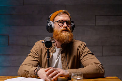 Bearded man with headphones at table, in front of microphone. podcast studio concept