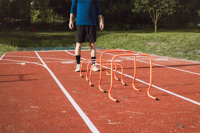 Blond boy in sportswear jumps over red obstacles to improve lower body dynamics