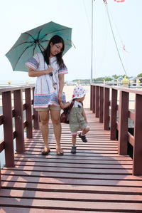Full length of mother and daughter standing on pier against sky
