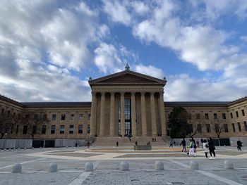 People in front of historical building against cloudy sky