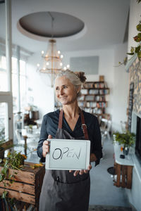 Female cafe owner showing open sign on digital tablet in coffee shop