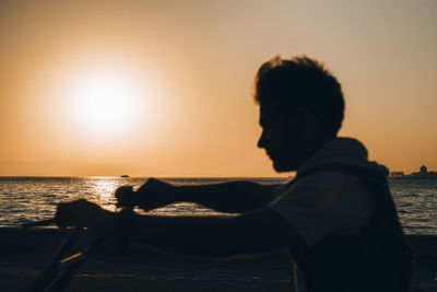 Silhouette man riding bicycle against sea during sunset