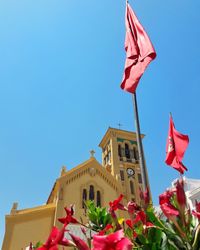 Low angle view of flags against buildings against clear blue sky