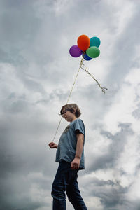 Low angle view of boy holding balloons against sky