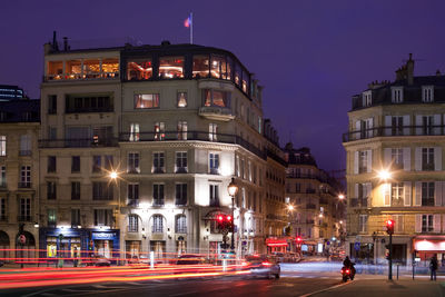 Illuminated light trails on street against buildings at night