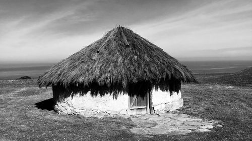 Hut on land by sea against sky