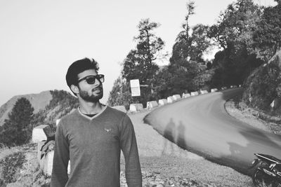 Portrait of young man standing on road against trees