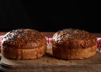 Baked round crispy sesame buns for burgers on brown wooden board, close up