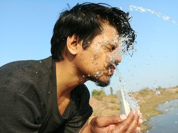 Close-up of man washing face against clear sky