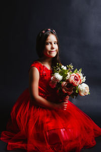 Portrait of girl holding bouquet while kneeling against black background