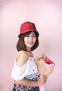 Portrait of smiling girl holding pink while standing against wall