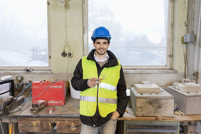 Portrait of confident young manual worker holding machine part in factory