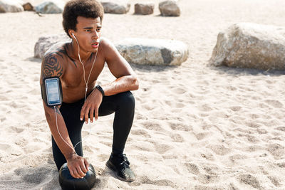 Shirtless young man looking away while relaxing on beach